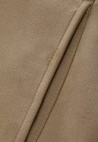 Tessuto scamosciato beige con una texture morbida, caratterizzato da una leggera lucentezza e da cuciture pulite lungo i bordi, che mette in risalto la sua superficie liscia.