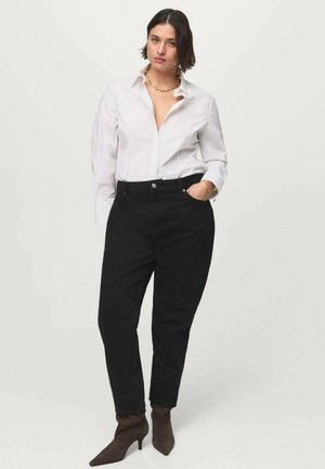 Pantalones de mezclilla negros con un corte relajado, combinados con una camisa blanca de botones. El atuendo se complementa con botas de tobillo puntiagudas marrones.