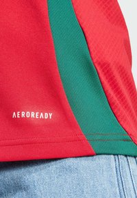 Camisa Aeroready roja y verde con tejido texturizado, que presenta paneles de color contrastante y un estampado de logo en el borde inferior.