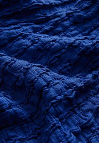 Blaues, strukturiertes Gewebe mit einem zerknitterten Muster, das unterschiedliche Tiefen und ein weiches, geschichtetes Aussehen zeigt. Ideal für vielseitige Anwendungen.