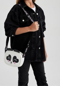 Bolso de panda blanco con acentos negros y grandes ojos en forma de corazón, con una correa rosa que tiene el texto "PLASTIC PANDA". Se lleva en estilo bandolera.
