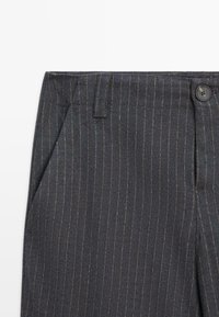 Pantaloni a righe grigio scuro con una vestibilità sartoriale, dotati di chiusura a un bottone, passanti per cintura e tasche laterali. Tessuto testurizzato con un leggero lucido.