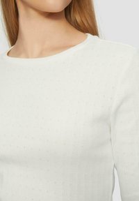 Hell gefärbter, gerippter Pullover mit rundem Ausschnitt, der kleine, dezente Punktmuster im Stoff aufweist. Weiche Textur.