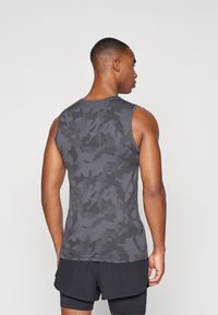 Grå, tettsittende ermeløs tank topp med et subtilt kamuflasjemønster og teksturert stoff. Brukt med svarte shorts, som viser et sporty design.