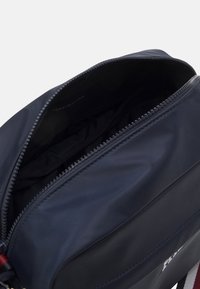 Granatowa torba Tommy Hilfiger z otwartym zamkiem błyskawicznym, ukazująca pustą komorę główną i czarne wnętrze.