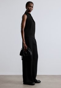 Fekete ujjatlan felső redős kialakítással, széles szárú fekete nadrággal és egy kis fekete bőrtáskával párosítva. Matt anyagok mindenhol.