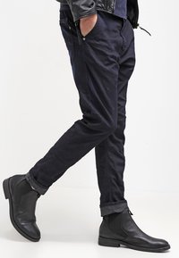Pantaloni di cotone blu scuro con orli risvoltati, abbinati a stivaletti neri in pelle con pannelli elastici laterali.