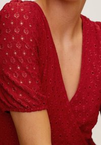 Rotes Kleid mit Puffärmeln, aus strukturiertem Stoff mit kleinen runden Ausschnitten. V-Ausschnitt-Design mit taillierter Taille.