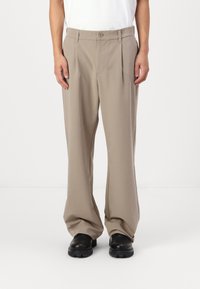 Beige wide-leg trousers in a smooth fabric with front pleats, a single button closure, and belt loops, paired with black sturdy footwear.