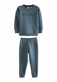 Dwuczęściowy zestaw dresowy w miękkim niebieskim materiale. Bluza z podwyższonym napisem "BAKER", natomiast spodnie mają gładkie i teksturowane akcenty po bokach.