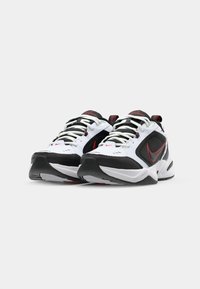 Pantofii sport Nike Air Monarch au un scheme de culori alb și negru, cu accente roșii, limbă căptușită, design cu șireturi și o talpă texturată pentru aderență.