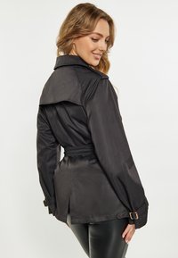Trench coat negru cu talie căptușită, guler pliat și o siluetă structurat. Prezintă manșete cu nasturi și o fantea în spate pentru un plus de libertate de mișcare.