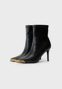 Black leather ankle boots with pointy toes, gold-accented toe caps, and slim high heels. Smooth texture and sleek design.