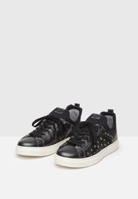 Mustat tenniskenkä, jossa on kiiltävä nahkavarsi, teksturoitu päällinen, mustat nauhat ja koristeelliset niitit sivuilla; pehmustettu nilkkasauma.