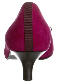 Scarpa con tacco alto in suede fucsia, con tacco affusolato e un dettaglio elastico marrone scuro lungo la parte posteriore per un supporto aggiuntivo.