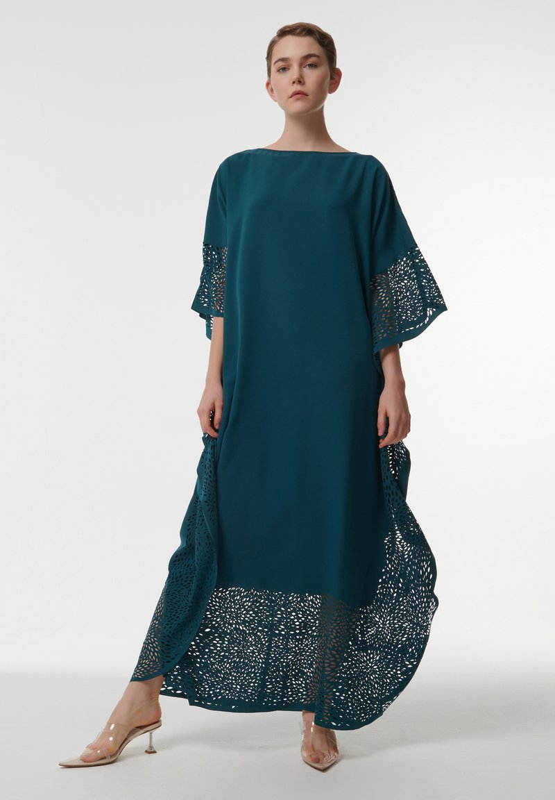 Vestido azul verdoso hecho de una tela ligera, con una silueta holgada, intrincados detalles de encaje en las mangas y el dobladillo, con acentos transparentes en la base.