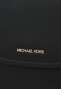 Superficie in pelle nera texture con piccolo logo dorato Michael Kors centrato vicino a un bordo cucito.