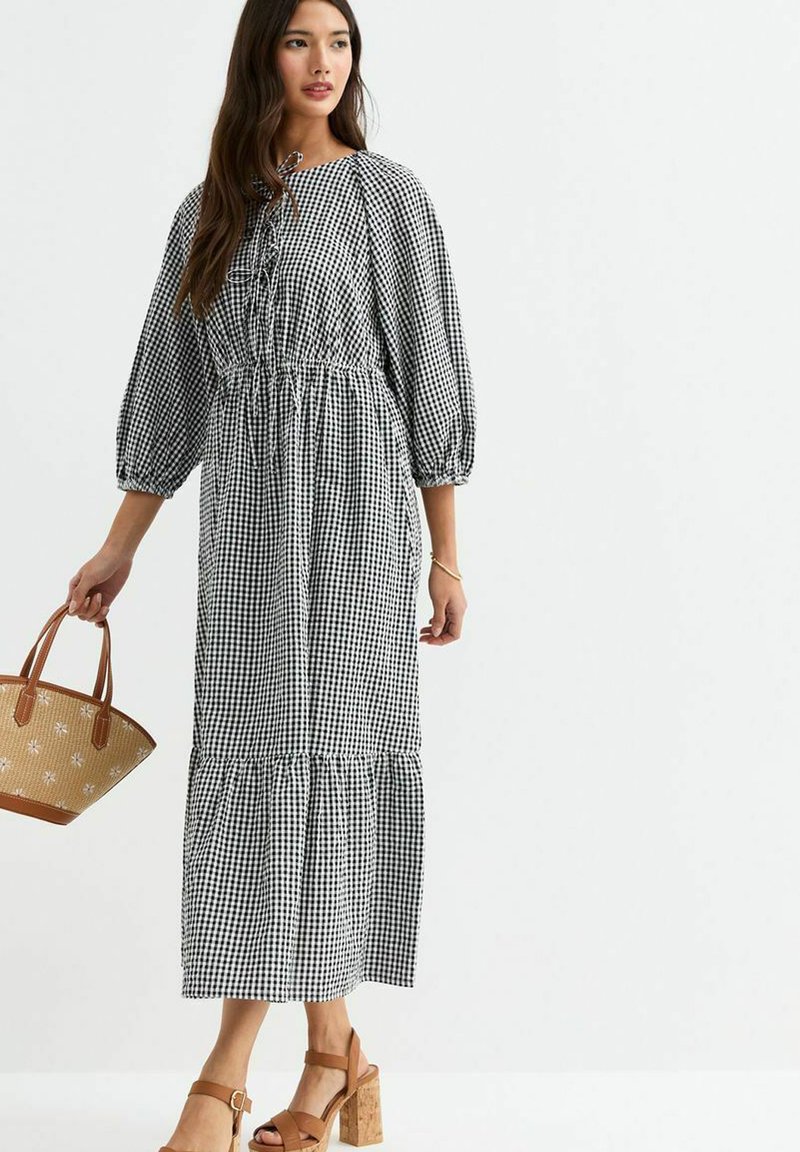 Robe vichy noir et blanc avec des manches bouffantes, taille cintrée et jupe à volants. Associée à un sac à main beige et des sandales à talons carrés.