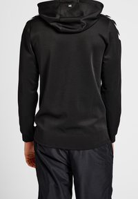 Sudadera negra con un diseño ajustado, mangas largas y un bolsillo tipo canguro. Cuenta con capucha y rayas blancas contrastantes en los hombros.
