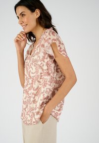 Korteblouse met korte mouwen in lichtroze met een rood paisleypatroon. De blouse heeft een V-hals en ruches bij de schouders.