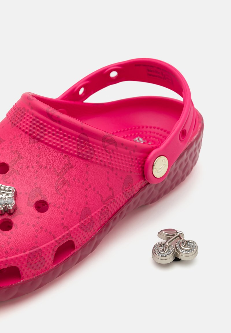 Zapatos de madera de color rosa brillante con una superficie texturizada, charms decorativos y agujeros de ventilación. Presentan una correa en el talón y un material flexible.