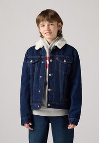 Giacca di jeans di colore blu scuro, con colletto in sherpa, accessori in metallo argentato e due tasche sul petto con dettagli di cucitura visibili.