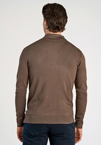 Brun stickad tröja med krage, långa ärmar och ribbad nederkant. Har en mjuk textur och en figursydd design. Baksidan visar sömdetaljer.