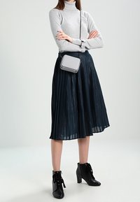 Šedý rolák, plisovaná černá midi sukně a černé kotníkové boty na šněrování. Malá šedá kabelka s černými detaily nošena přes tělo.