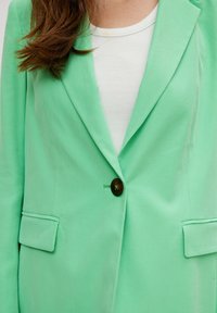 Mintgrüner Blazer mit strukturiertem Design, Ein-Knopf-Verschluss und zwei Fronttaschen. Hergestellt aus glattem Stoff, bietet eine weiche Textur.