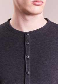 Mörkgrå, ribbad långärmad tröja med rund hals och fem svarta knappar längs framplåten. Slät textur.