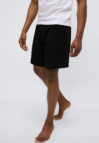 Pantalones cortos negros hechos de un material suave, con un ajuste relajado, bolsillos laterales y un diseño simple y sin adornos. Combinados con una camiseta blanca.