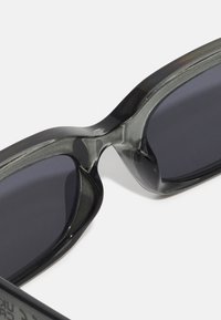Gafas de sol con un marco de plástico negro brillante, diseño envolvente y lentes oscuros. El puente presenta una conexión suave entre los lentes.