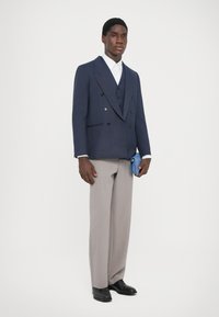 Tengerészháromsoros zakó, világosszürke nadrág, fehér ing, fekete cipő, kék clutch táska. Sima anyag klasszikus szabásminta részletekkel.