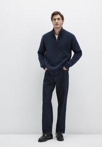 Navy zip-up fleece pullover with a relaxed fit, paired with dark denim straight-leg jeans and black lace-up shoes. Plain design.