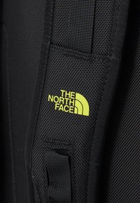Sangle en tissu noir arborant un logo vert avec trois lignes courbes et le texte "THE NORTH FACE" en lettres majuscules.