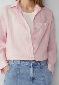 Chemise en lin rose clair à boutons avec une coupe décontractée, dotée d'une poche plaquée et de boutons visibles. Associée à un jean en denim taille haute.