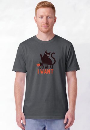 Mann trägt graues T-Shirt mit schwarzer Katze, die eine Krabbe hält, und Text mit der Aufschrift "I do what I want" in schwarzen und orangefarbenen Buchstaben.