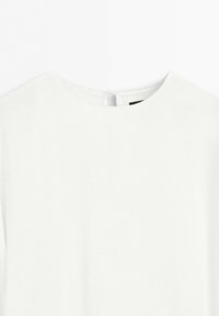 Witte blouse met ronde halslijn en naaddetail bij de achtersluiting tegen een effen achtergrond.