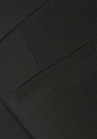 Zwarte stofclose-up met een soepel textuur en een subtiele glans, een diagonaal stikpatroon, en een klein zakdetail aan de zijkant.