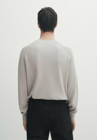 Pull en maille côtelée gris clair à manches longues, col rond et coutures raglan, associé à un pantalon noir. Texture lisse et coupe décontractée.