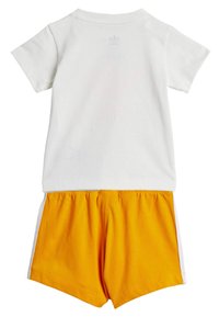 T-shirt en coton blanc à manches courtes, associé à un short jaune avec une taille élastique et des accents blancs sur les côtés.