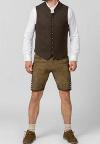 Braune Wollweste mit Knopfverschluss, kombiniert mit hellbraunen Lederhosen mit Stickerei und Seitentaschen. Braune Socken und Schuhe runden das Outfit ab.