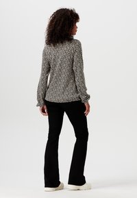 Blusa a maniche lunghe con un motivo astratto in bianco e nero, tessuto leggero, polsini arricciati, abbinata a pantaloni neri svasati e scarpe casual.