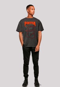 Schwarzes Grafik-T-Shirt mit einem roten und grauen Schlangendesign und dem Text "PANTERA". Kombiniert mit schwarzen Jogginghosen und schwarzen Turnschuhen.
