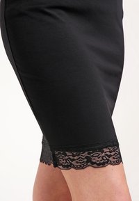 Czarna ołówkowa spódnica wykonana z gładkiego materiału z delikatną czarną koronką u dołu, o prostym kroju i długości do kolan.