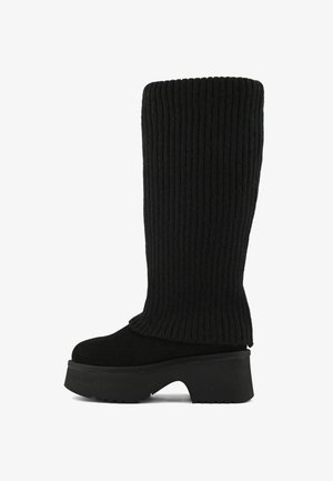 Bota negra de media caña con tacón grueso y parte superior de punto acanalado que se extiende desde la plantilla hasta la parte superior del caño.