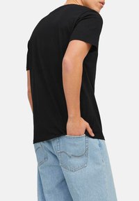 Black cotton t-shirt with short sleeves, standard crew neck, and a relaxed fit, worn with light blue denim jeans featuring back pockets.