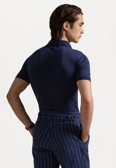 Navy blue short-sleeved polo shirt paired with blue pinstriped trousers, featuring a sleek, tailored fit and minimal detailing. Back view.