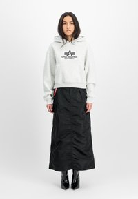 Felpa grigia in cotone con logo nero, abbinata a una lunga gonna nera in nylon, caratterizzata da una texture liscia e tasche laterali, completata da stivali neri.