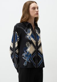 Schwarzes Hemd mit langen Ärmeln, das ein geometrisches Muster in Blau und Beige aufweist, mit Knopfleiste und glatter Stofftextur.